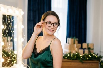 Femme élégante portant des lunettes écaille de tortue et une nuisette en satin vert émeraude avec dentelle pour les fêtes